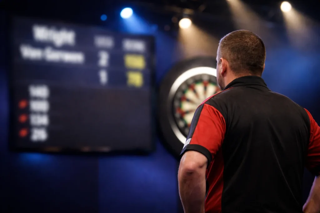 Scorebord met darts-statistieken naast een dartbord op een professioneel toernooi